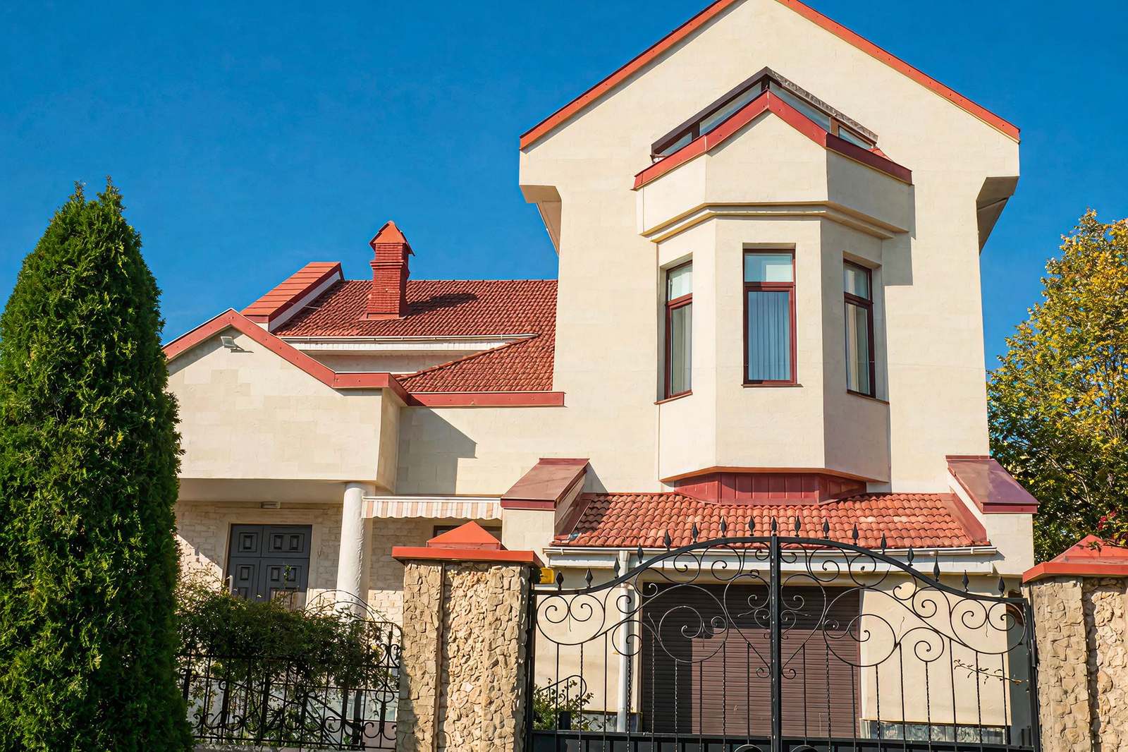 Vedere de la poartă: casă cu acoperiș roșu și fațadă din piatră flexibilă deschisă